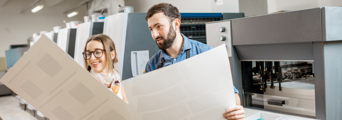 Abbildung Zwei Techniker stehen vor einem Drucker und begutachten den Ausdruck 