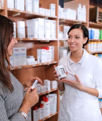 Abbildung eine Apothekerin vor dem Medikamentenregal mit Medikament in der Hand spricht mit einer anderen Frau