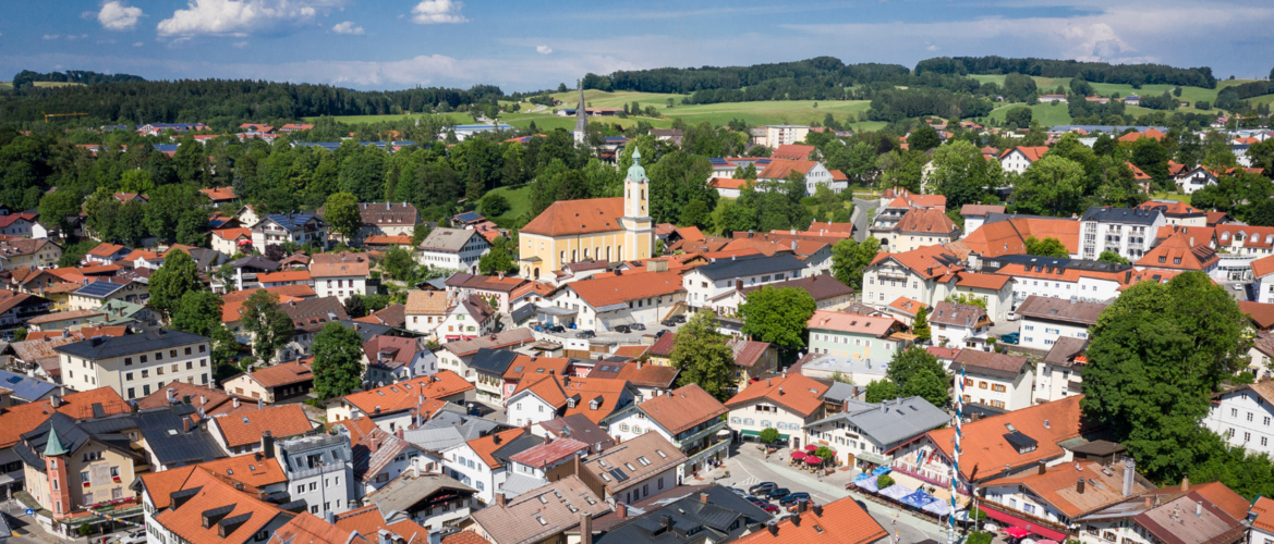 Abbildung Flugaufnahme der Stadt Miesbach mit vielen Häusern und großer grünen Wald und Wiesenfläche 