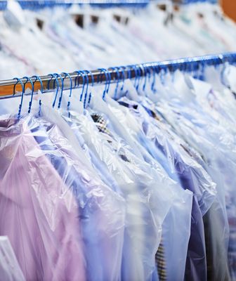Abbildung verschiedene Kleidung in Schutzhüllen auf Kleiderbügeln und Kleiderstangen