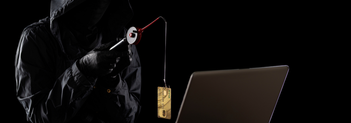 Abbildung dunkle bekleidete Person sitzt mit einer Angel und einer Bankkarte als Lockmanöver vor einem Laptop