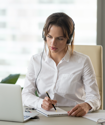 Abbildung eine Frau in weißer Bluse mit Kopfhörer sitzt vor Laptop mit Stift und Block
