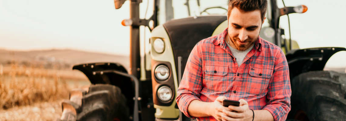 Abbildung ein mann lehnt vor einem Traktor und schaut aufs Handy 