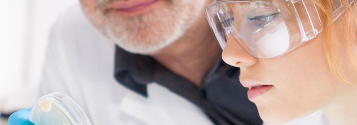 Abbildung zwei Menschen mit weißem Kittel und Schutzbrille schauen sich im Labor eine Chemieprobe an 