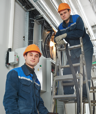 Abbildung zwei Arbeiter in Arbeitskleidung und Schutzhelm mit einer Leiter vor einer elektronischen Anlage