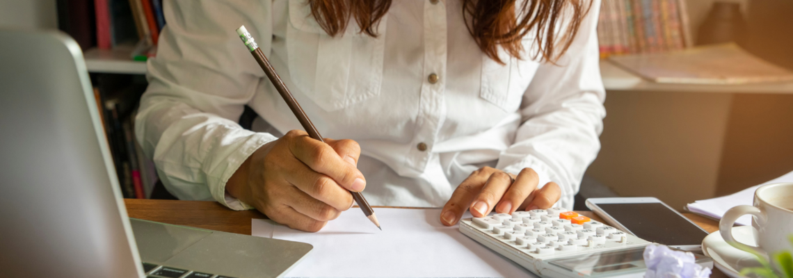 Abbildung Frau sitzt an einem Schreibtisch mit einem Taschenrechner und füllt Dokumente aus 