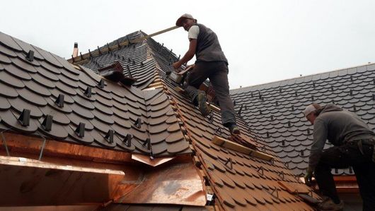 Abbildung zwei Männer die ein Dach mit schwarzen Dachpfannen decken