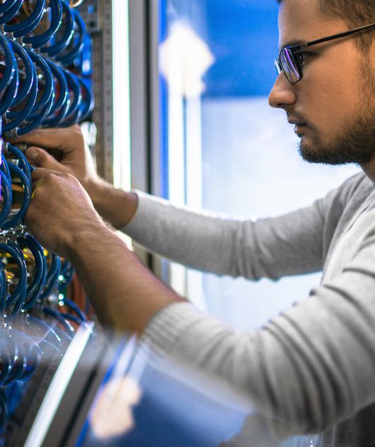 Abbildung Mann mit Brille steckt verschiedene Lan Kabel in einem Serverschrank ein