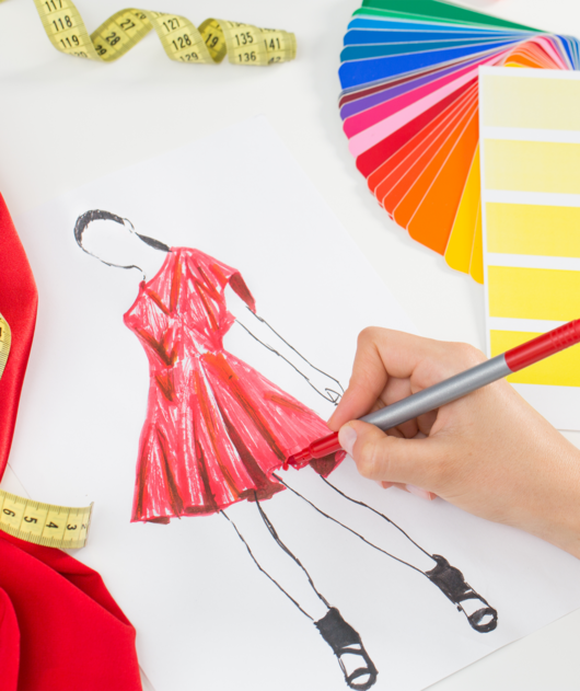 Abbildung Hand mit Stift, die eine rotes Kleid zeichnet, daneben liegen Farbkarten und ein Maßband
