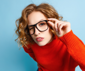 Abbildung eine junge Frau mit Brille schaut genau durch das Brillenglas