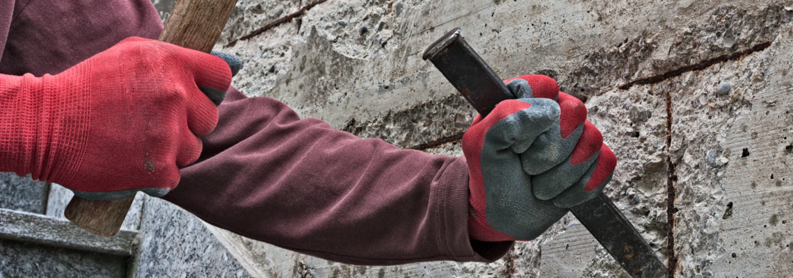 Abbildung zwei Hände bearbeiten mit Steinmeißel und Hammer eine alte Steinwand 