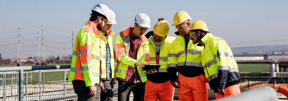 Abbildung sechs Baustellenarbeiter stehen im Halbkreis und schauen auf ein Tablett