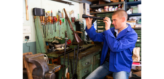 Abbildung Mann im blauer Arbeitsjacke in einer Werkstatt, der Teilstück einer Büchse in den Händen hält