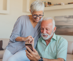 Abbildung zwei Senioren sitzen vor einem Smartphone und schreiben Nachrichten