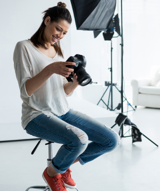 Abbildung leger gekleidete Frau sitzt mit einer Kamera in den Händen im Fotostudio