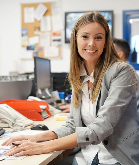 Abbildung Frau am Schreibtisch im Büro dahinter eine Person am PC