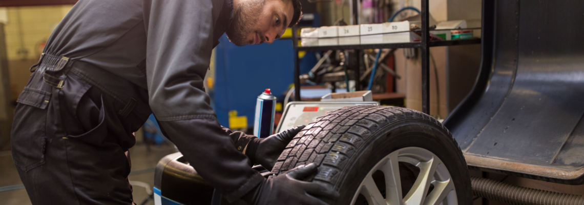 Abbildung ein Mann untersucht in einer Werkstatt einen Reifen auf einer Halterung  