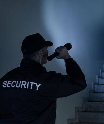 Abbildung Mann mit Security Jacke leuchtet mit einer Taschenlampe in einen dunklen Gang