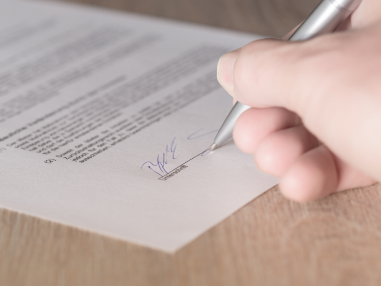 Abbildung eine Person unterschreib mit einem Kugelschreiber einen Vertrag