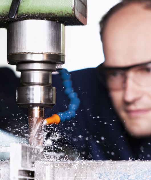 Abbildung Mann mit Schutzbrille arbeitet an einer Metallmaschine