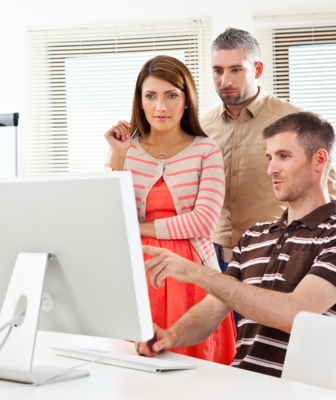 Abbildung ein Paar steht neben einem jungen Mann, der vor einem weißen PC sitzt und auf den Bildschirm deutet