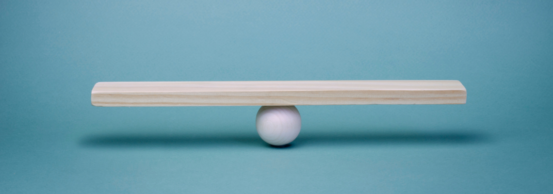 Abbildung eine Kugel auf der ein Holzstück balanciert vor einem Türkisen Hintergrund 