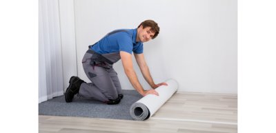 Abbildung Mann rollt Teppich auf Boden in einem Raum aus