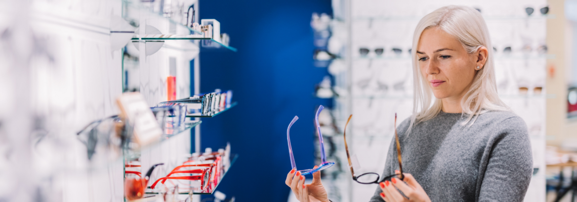 Abbildung eine Frau schaut sich in einem Brillenladen zwei Brillen genauer an 