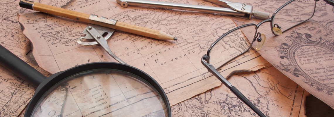 Abbildung auf mehreren alten Karten liegen eine Brille eine Lupe Stifte und andere Dinge