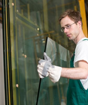 Abbildung Mann mit grüner Latzhose und Arbeitshandschuhe nimmt eine Glaswand aus den Glasständer