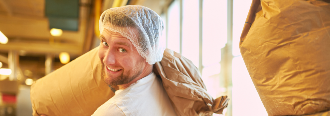 Abbildung ein Mann mit Haarnetz trägt einen Sack voll Mehl 
