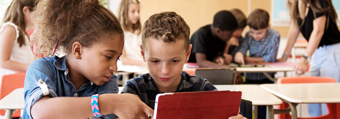 Abbildung zwei Kinder sind in einem Klassenzimmer und lernen gemeinsam auf einem Tablet  