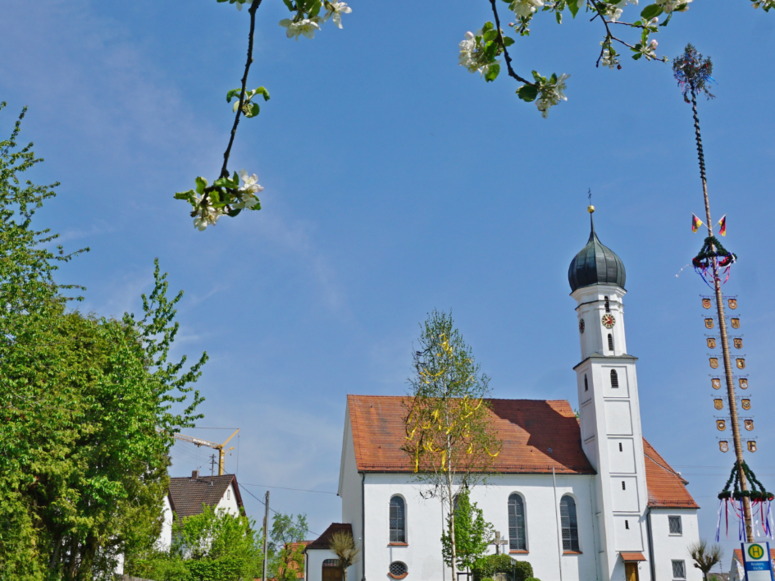 Abbildung Blick über eine Wiese hin zu einer Kappelle mit Kirchturm