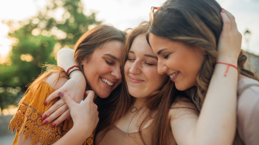 Abbildung drei Freundinnen halten sich freundschaftlich im Arm und lächeln dabei