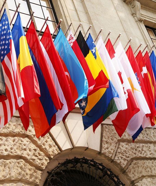 Abbildung mehrere Länderflaggen nebeneinander an einem Gebäude hängend