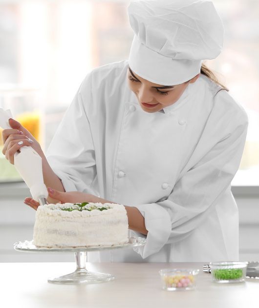 Abbildung Frau mit Kochhaube und weißem Kochgewand garniert mit einem Spritzbeutel eine Torte