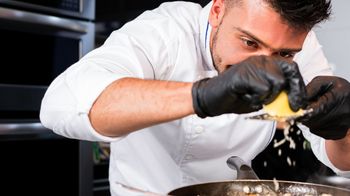 Abbildung ein Koch reibt Parmesan über einer Pfanne