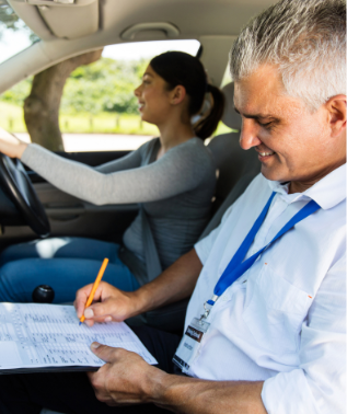 Abbildung Eine Fahrschülerin am Steuer und ein Fahrlehrer, der sich Notizen macht, in einem rechtsgesteuerten Fahrzeug